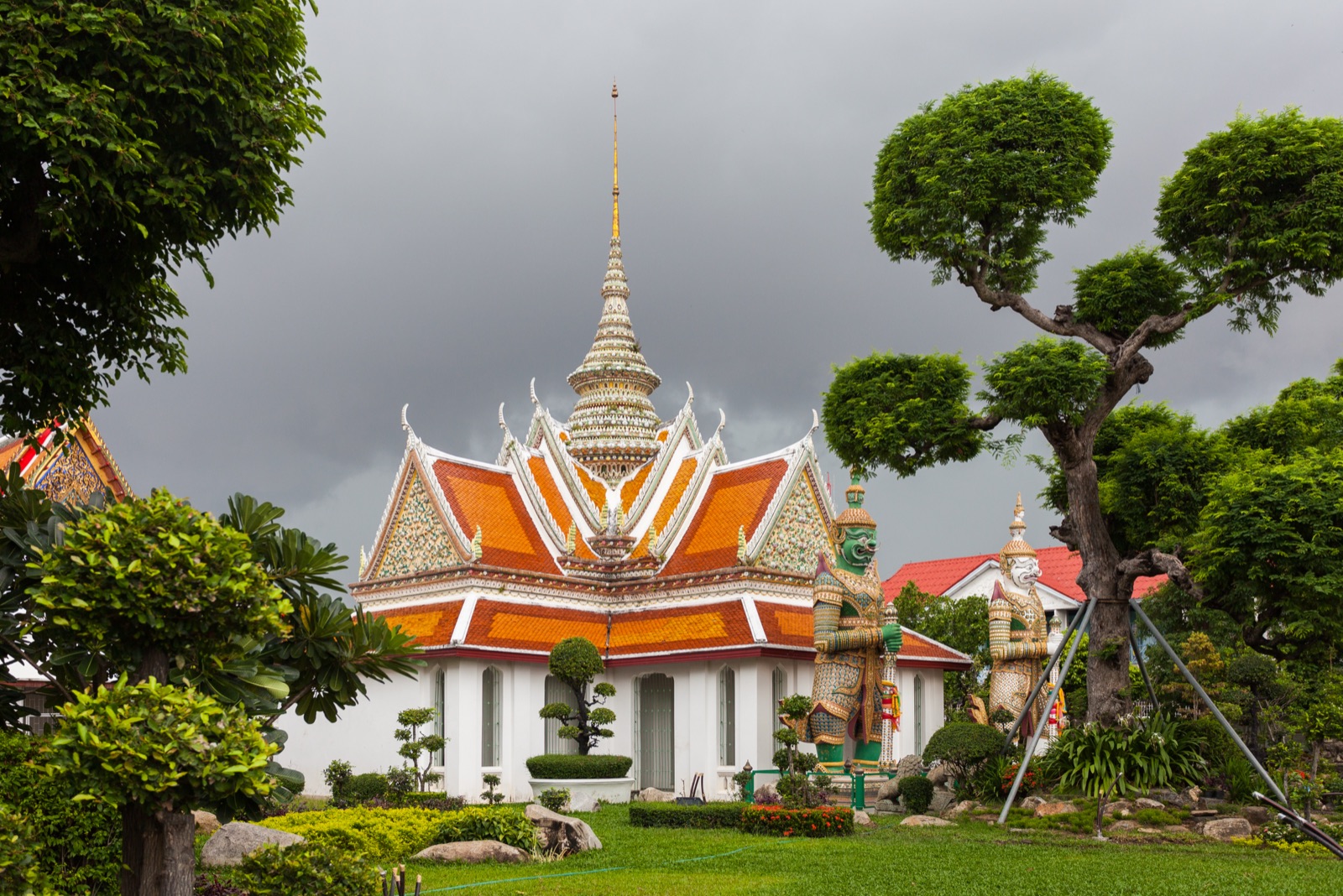 Wat Arun Temple in Bangkok among trees, under sky loaded
